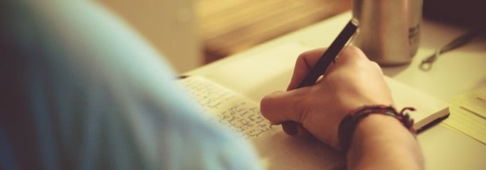Image shows a writer writing in a notebook. 