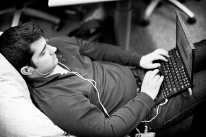 Hình ảnh cho thấy một người đàn ông trong một chiếc áo nằm lại và sử dụng một máy tính xách tay.