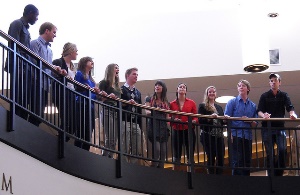 Image shows students and academics standing around at the top of a stairwell. 